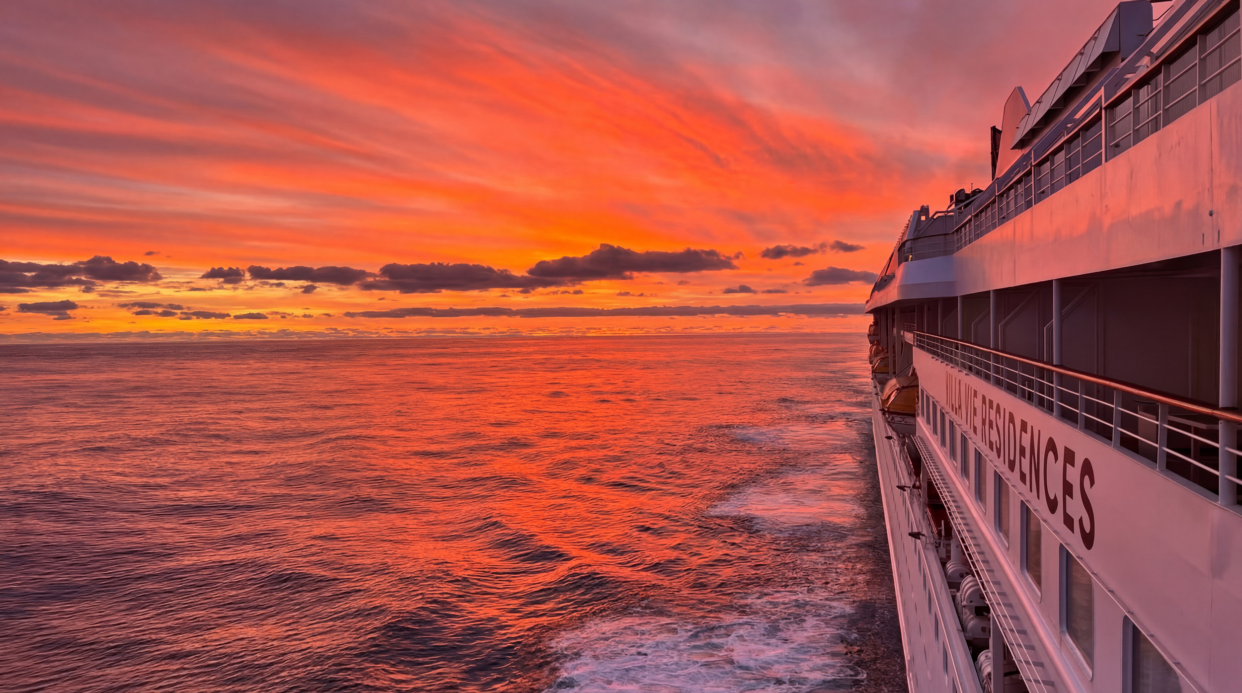 The Villa Vie Odyssey at sea under a red sunset, its name along the hull